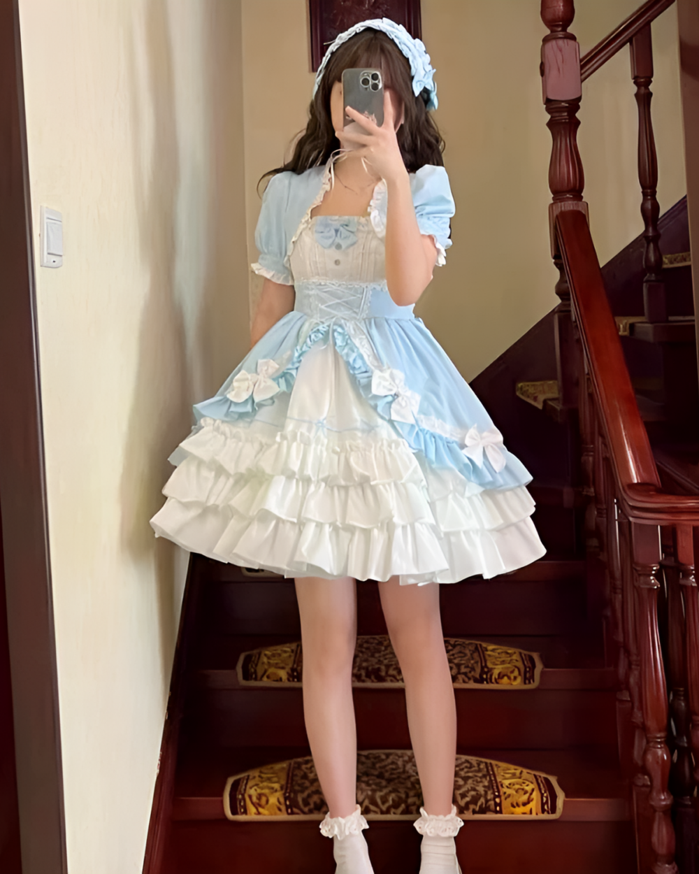 A person wearing a light blue Hime Lolita Dress Collection layered with ruffles and lace, standing on a staircase.