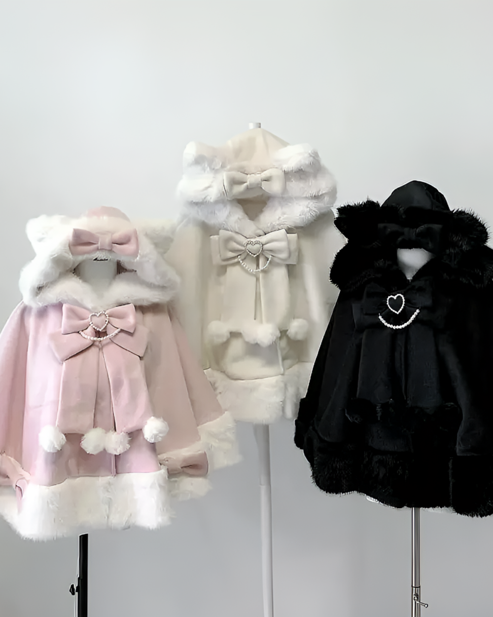Two Hooded Fluffy Cat Eared Cloaks, one pink and one white, alongside a black Cat Eared Cloak, displayed on a mannequin.