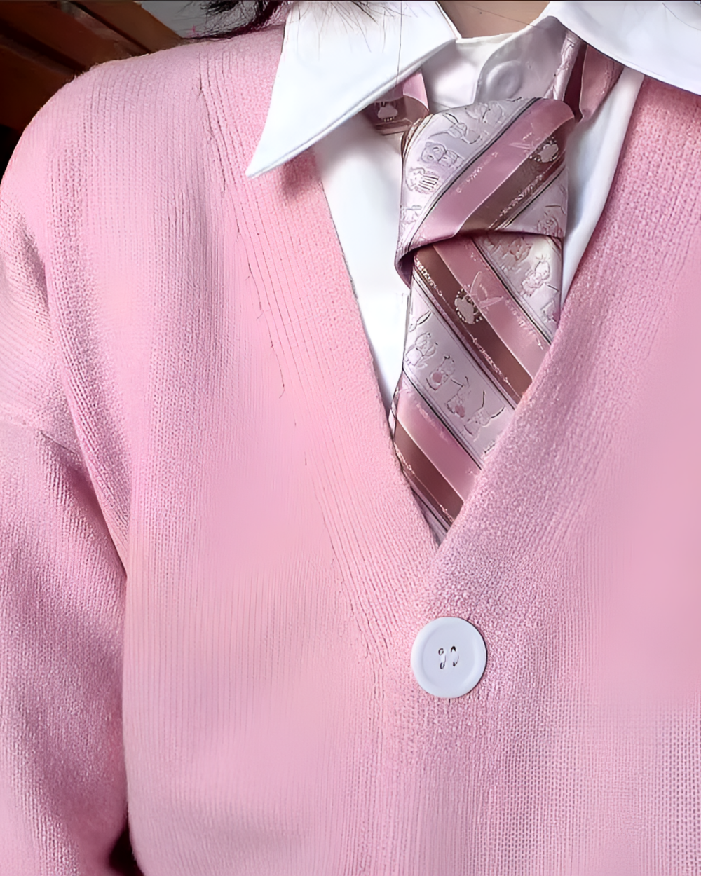 Close-up of a pink JK cardigan sweater worn over a collared shirt and tie. The sweater features a V-neck and button closure.