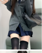 Woman wearing a gray JK cardigan sweater with a pleated skirt and black socks.
