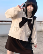 Cream-colored Japanese knitted cardigan with a black bow and button details, worn by a young woman.