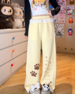 Yellow Kaomoji Paw Print Pants worn by a person, featuring paw print details.