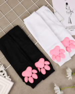 Black and white 3D cat paw sleeves with pink paw details, lying on a surface with flowers.