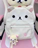 Close-up of a white Kawaii Bear Backpack by Jojifuku, featuring a bear face design and front pocket. A small bear plush is beside it.