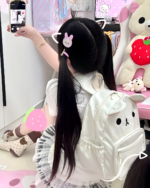 Woman with long dark hair wearing a white Kawaii Bear Backpack by Jojifuku, with pink strawberry plushie nearby.