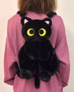 Person wearing a pink sweatshirt with a black Kawaii Cat Plushie Backpack attached. The backpack features large yellow eyes.