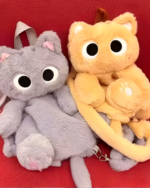 Two Kawaii Cat Plushie Backpacks, one gray and one orange, shown close-up. Soft plush toy design with large eyes.