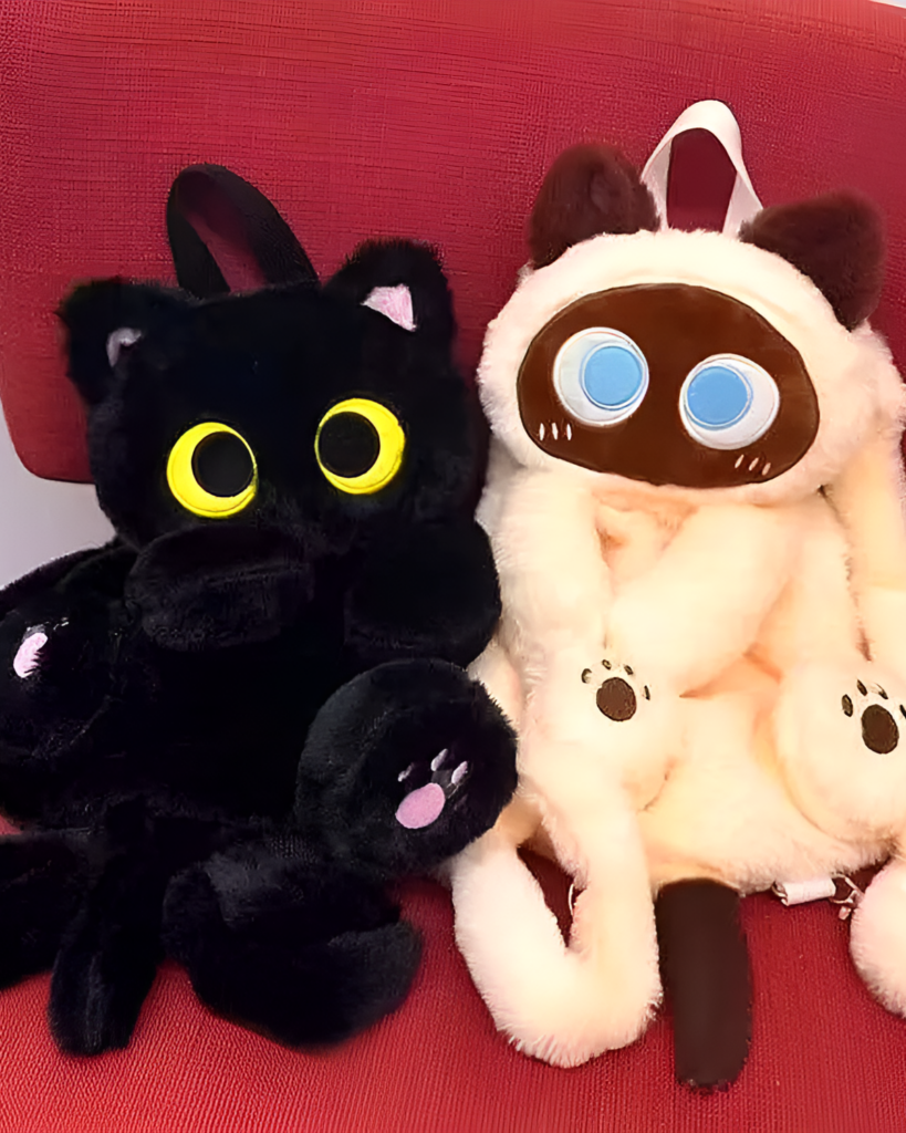 Two Kawaii Cat Plushie Backpacks, one black and one beige, sit against a red background. They have large eyes and paw details.