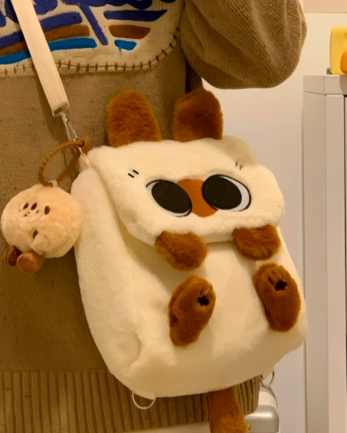 Close-up of a white and brown Kawaii Siamese Cat Plush Backpack hanging on a rack. Features large, expressive eyes.