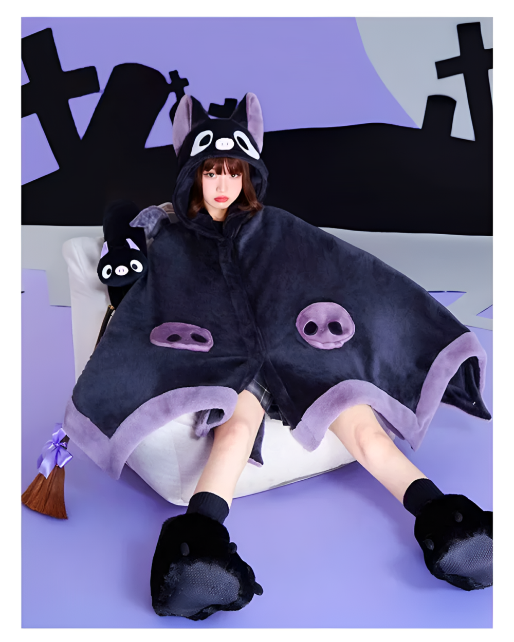 A person wearing a black Kawaii Winged Eared Plush Cape with white trim and bat-like ears. Includes matching plush slippers.
