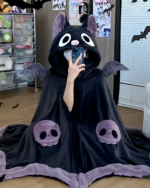 Person wearing a black Kawaii Winged Eared Plush Cape with skull details. The cape has purple trim and wings.