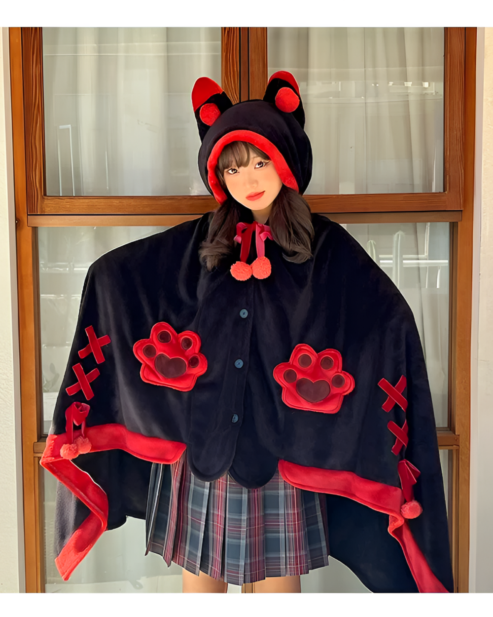 A person wearing a black Kawaii Winged Eared Plush Cape with red accents and paw prints. The cape has a hood with ears.