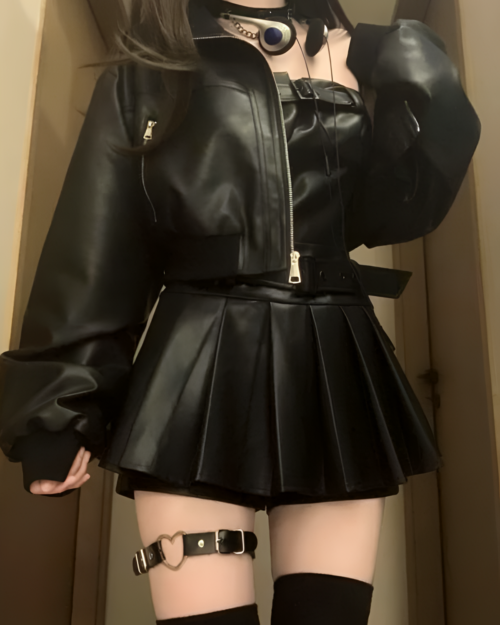 Black vegan leather two piece set: jacket and pleated mini skirt, with thigh-high stockings and accessories.