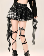 Model wearing a black and white plaid goth punk skirt with lace and chain details. The skirt features a mini length and unique design.