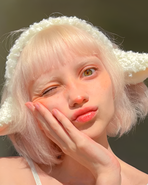 Close-up of a person wearing a fluffy white lamb ears headband. The headband features soft, curled lamb ears.