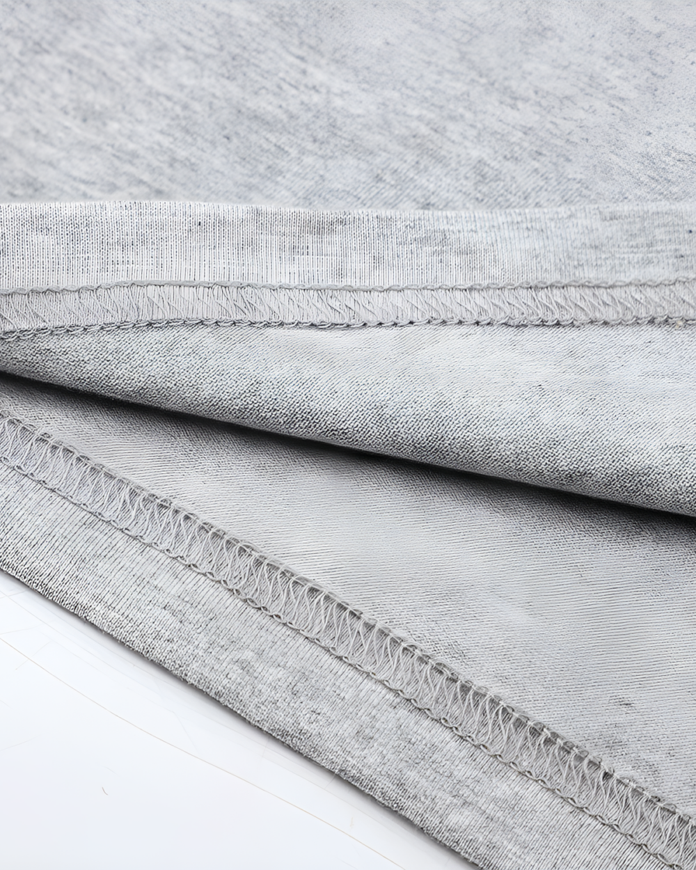 Close-up of a gray Kuro Neko T-Shirt showing detailed stitching on the hem. Soft fabric texture visible.