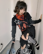 Woman posing with a black skull print shirt, long sleeves, and ripped stockings.