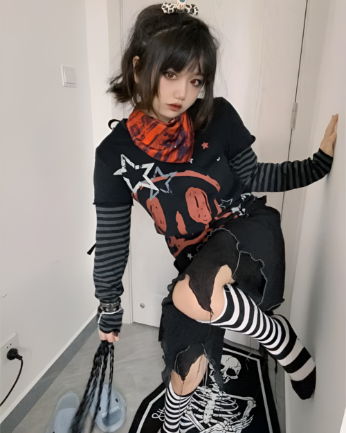 Woman posing with a black skull print shirt, long sleeves, and ripped stockings.