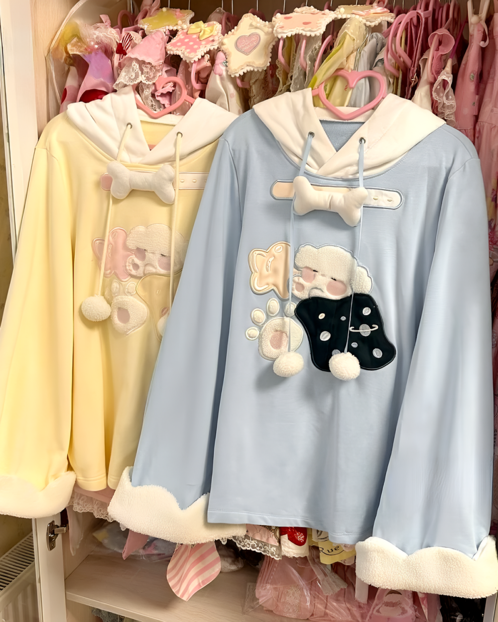 Two Jojifuku hoodies hanging in a closet, one yellow and one blue, both with bear embellishments.