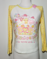 Mezzo Piano cake T-shirt with long sleeves, featuring a colorful cake and character graphic. Yellow and white design.