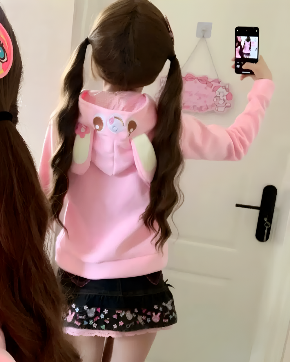 Back view of a woman wearing a pink Mezzo Piano Yume Kawaii hoodie with bear ears, styled with a dark skirt.