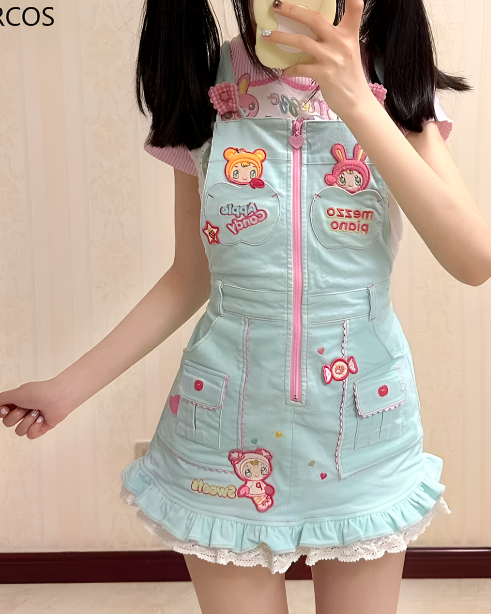 A girl wearing a light blue Mezzo Piano dress with pink accents and cartoon appliques. The dress has a ruffled hem and shoulder straps.