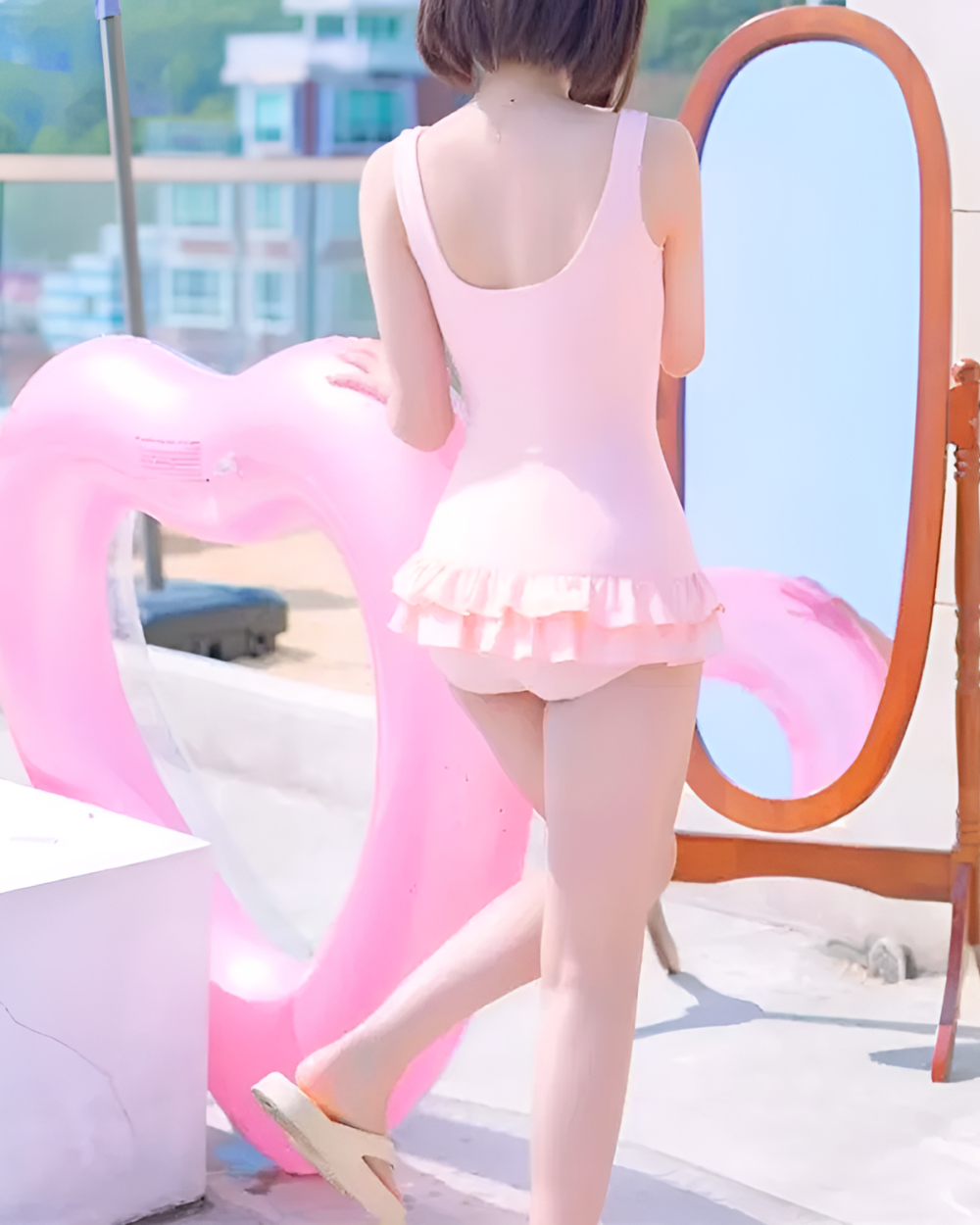 Woman wearing a pink animecore swimsuit with a ruffled waist, posing in front of a mirror with a flamingo float.
