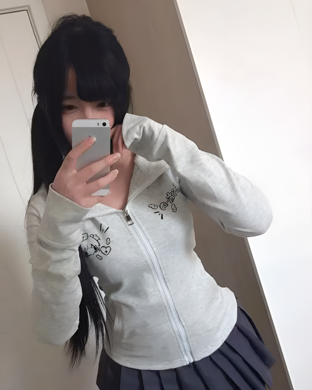 Person wearing a grey zip-up Yami Kawaii hoodie with a cat design, paired with a plaid skirt.