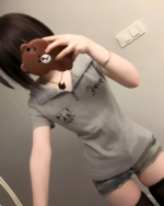 Person wearing a gray Yami Kawaii hoodie with a cat graphic and denim shorts. The hoodie features a zip-up design.