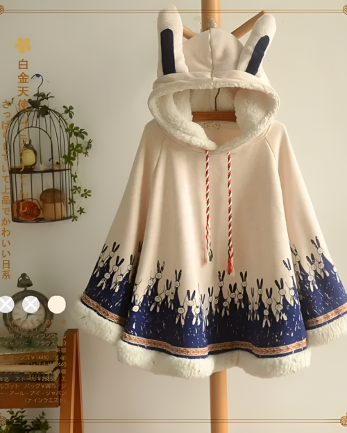 Beige bunny fleece cape with a patterned hem and hood. Features bunny ears and a soft, plush texture.