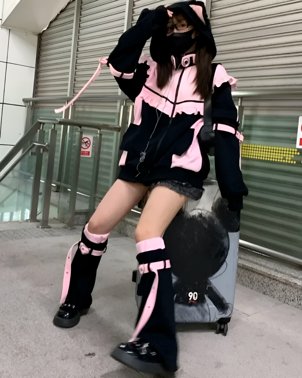 Model wearing a Neko Frill Zip Hoodie in pastel goth aesthetic. Features a cat-ear hood and frill details. Pink and black color scheme.