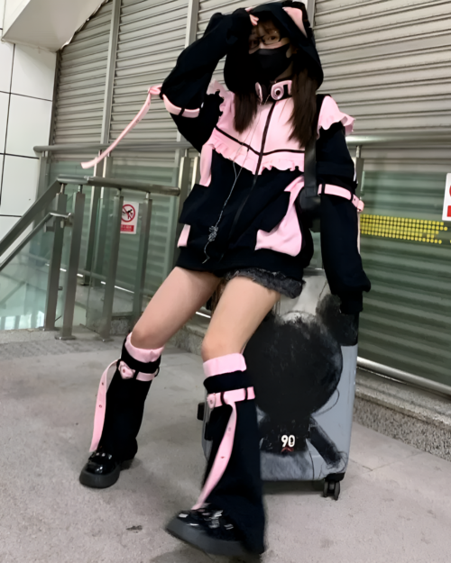 Model wearing a Neko Frill Zip Hoodie in pastel goth aesthetic. Features a cat-ear hood and frill details. Pink and black color scheme.