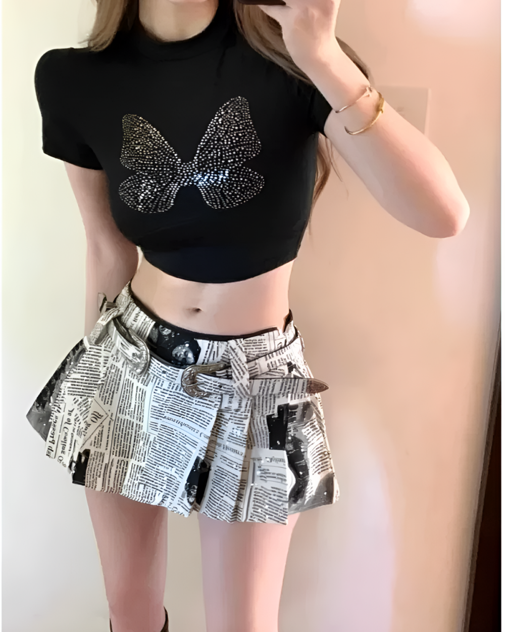 Woman wearing a black butterfly top and a grey newspaper print Y2K pleated skirt, styled as a trendy outfit.