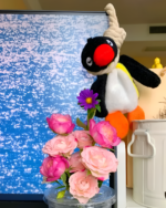 Close-up of a Noosed Penguin Keychain with flowers. Features a black and white plush penguin with a red beak.