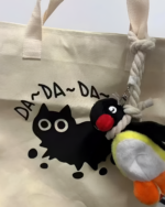 Close-up of a beige tote bag with a yellow and black graphic and a hanging Noosed Penguin Keychain.