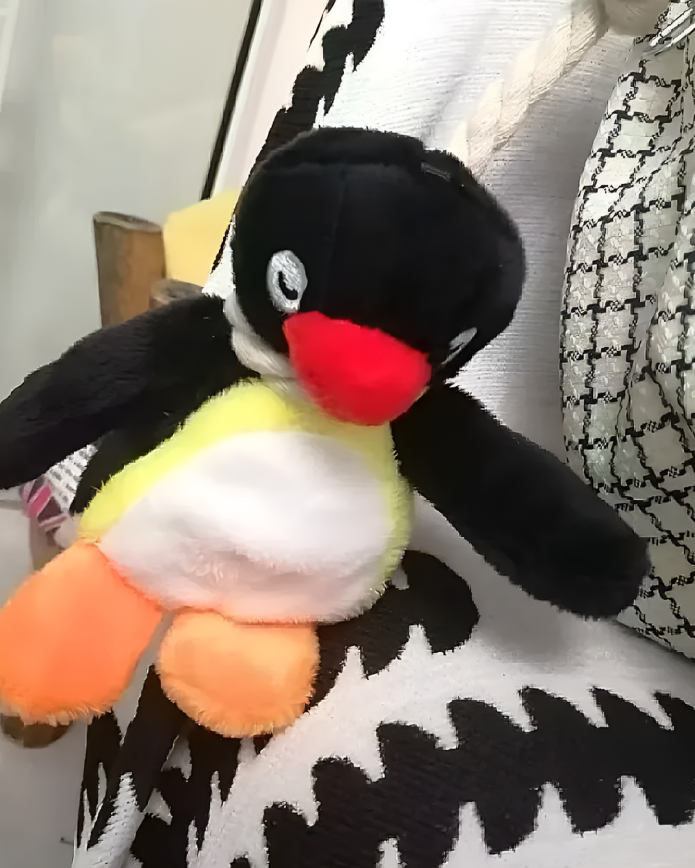 Close-up of a black and white Noosed Penguin Keychain with a red beak and orange feet, resting on a patterned fabric.