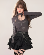 Model wearing a dark grey long sleeve top and black star chain skirt with a layered ruffle hem. The skirt features a chain belt.