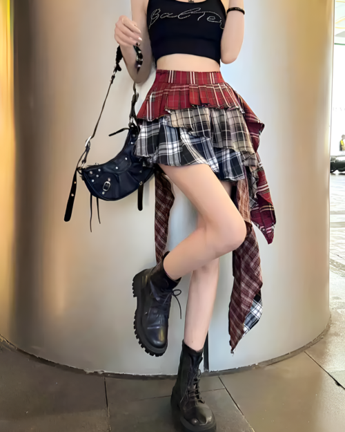 Model wearing a red and black patched pleated skirt with a grunge aesthetic, paired with boots and a handbag.
