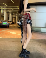 Woman wearing a patched pleated skirt with a grunge aesthetic, paired with a black top and boots. A fashionable layered skirt.