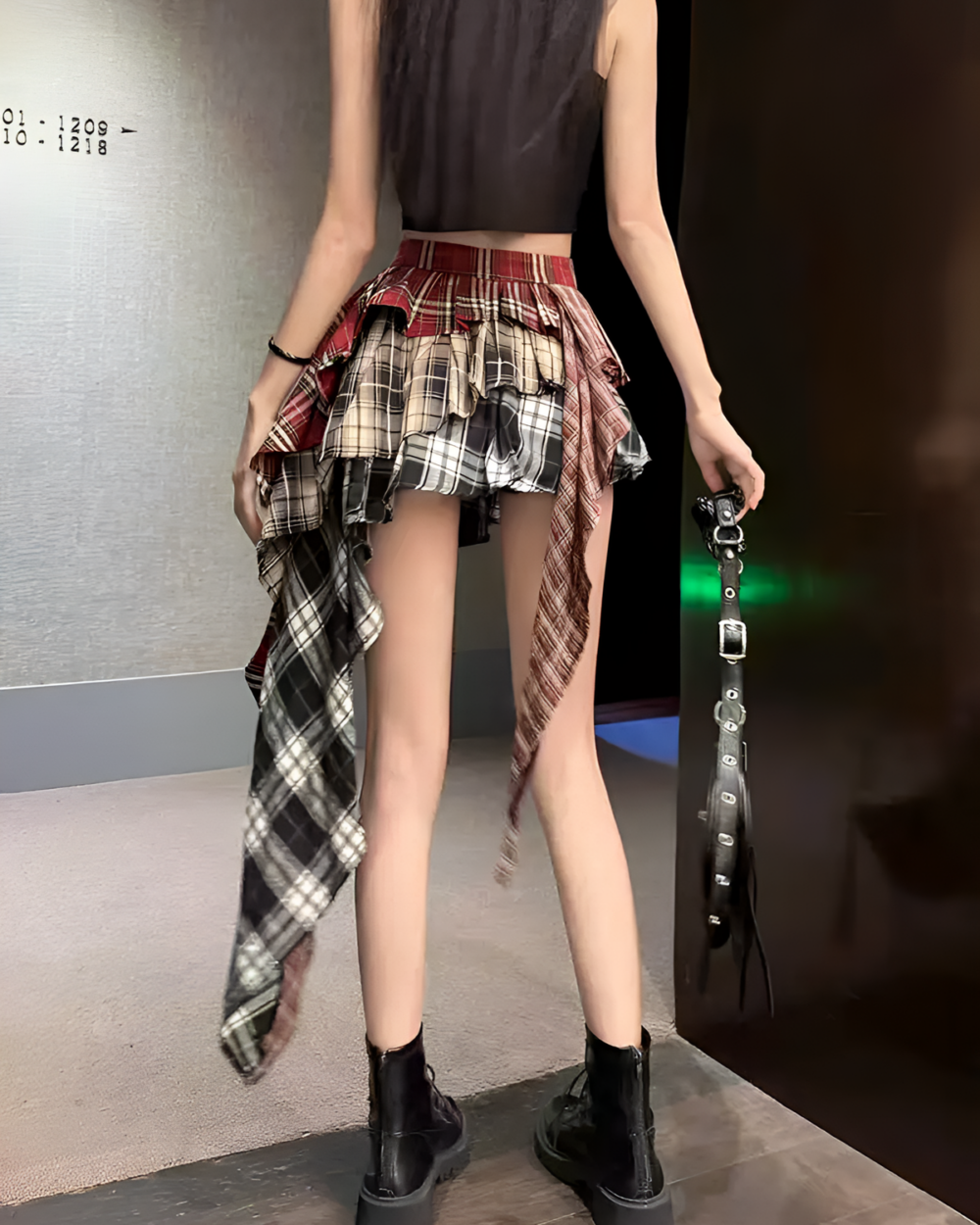 Woman wearing a red and black patched pleated skirt with a grunge aesthetic, paired with a black top and boots.