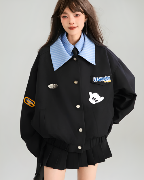 Woman wearing a black Patchy Jacket with colorful enamel pins and a striped shirt underneath. Preppy aesthetic outerwear.