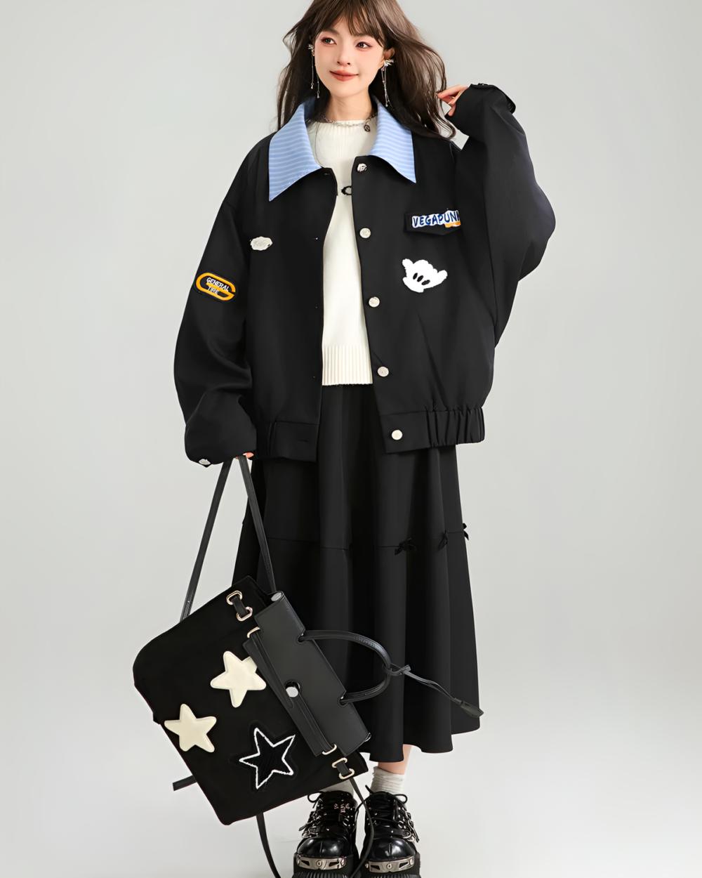 Woman wearing a black Patchy Jacket with colorful patches and a blue collar. It has a preppy aesthetic and is paired with a black skirt.