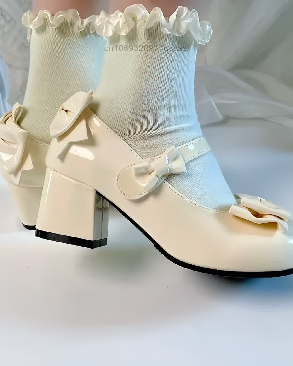 Close-up of beige Petal Block-Heel Mary Janes with bow details and a block heel. The shoes are on a light textile surface.