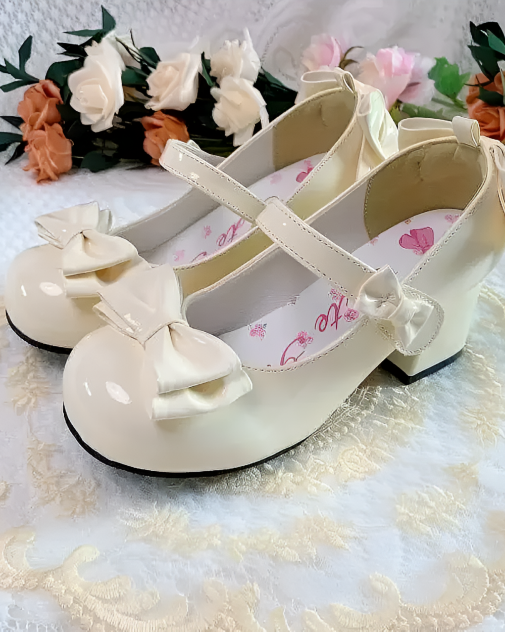 Cream-colored Petal Block-Heel Mary Janes with a bow detail, presented against a floral backdrop.