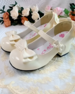 Cream-colored Petal Block-Heel Mary Janes with a bow detail, presented against a floral backdrop.