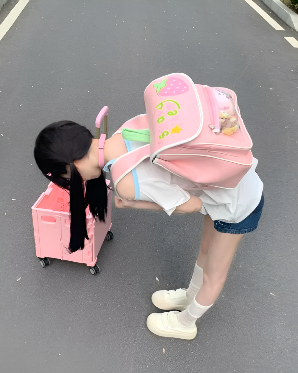Pink strawberry ita bag backpack held by a young person outdoors.