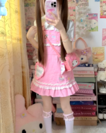 Model wearing a pink strawberry mini dress with lace trim and a crossbody bag. Jojifuku aesthetic.