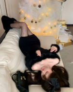 Woman wearing a black Plush Christmas Dress with faux fur trim, near festive decorations.