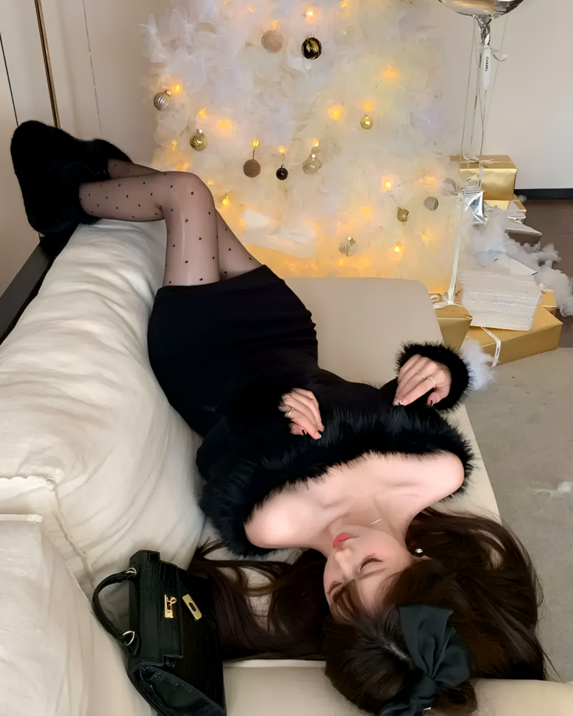Woman wearing a black Plush Christmas Dress with faux fur trim, near festive decorations.