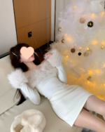 Woman wearing a Plush Christmas Dress, sitting on a bed next to a Christmas tree.